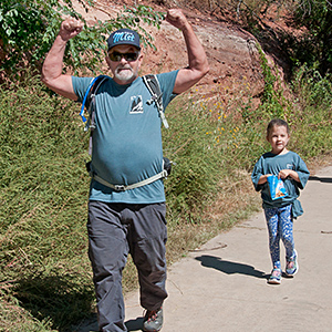 Man walking on sidewalk with water pack on and kid walking behind him